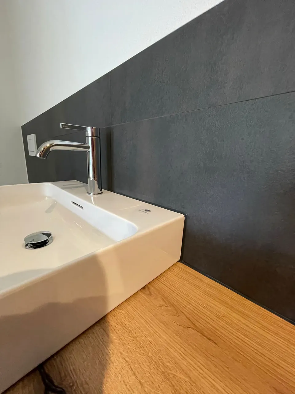 Lavabo vor dunkler Wandfliese mit Holzablage