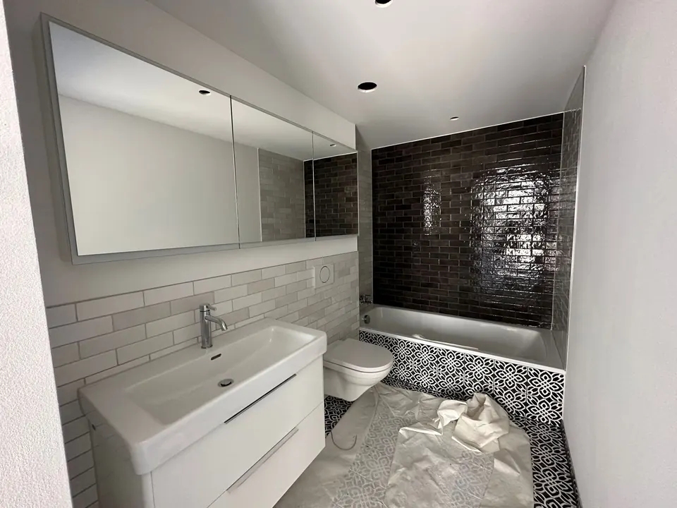 Badezimmer mit Spiegelschrank und dunklen Glanzfliesen